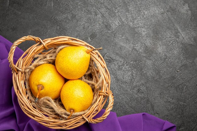 Top close-up view pears in basket basket of three ripe pears on the purple tablecloth on the dark table