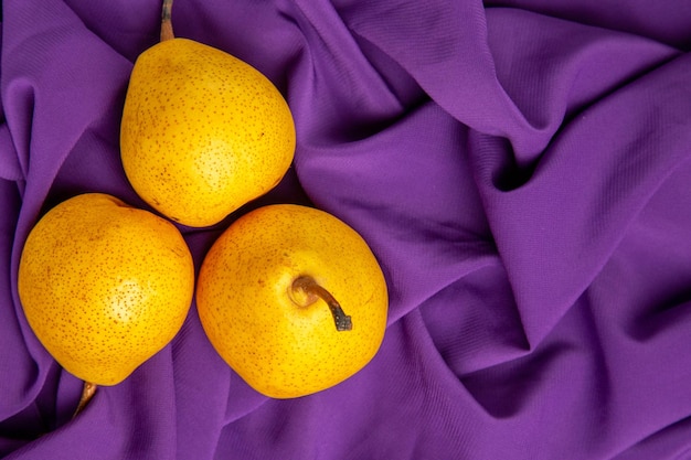 Top close-up view pears on the tablecloth on the left side of the table three appetizing pears on the purple tablecloth