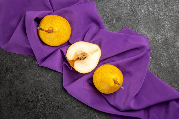 テーブルクロスの上のクローズアップビュー梨2つの黄色の梨と暗いテーブルの紫色のテーブルクロスの半分の梨