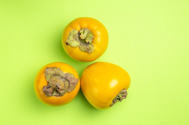 Free photo top close-up view persimmons three appetizing persimmons on the green table