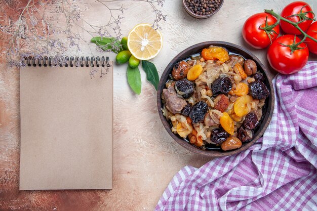 Top close-up view pilaf an appetizing rice dried fruits black pepper tomatoes cream notebook