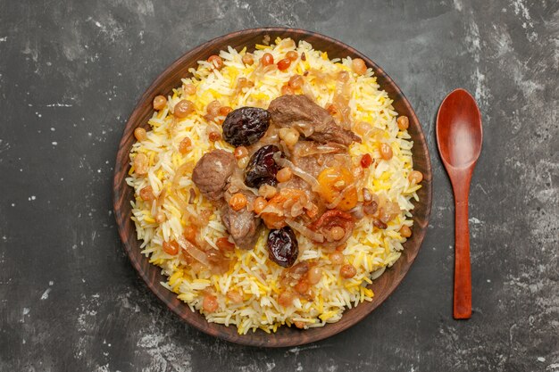 Top close-up view pilaf dried fruits rice and meat in the bowl wooden spoon