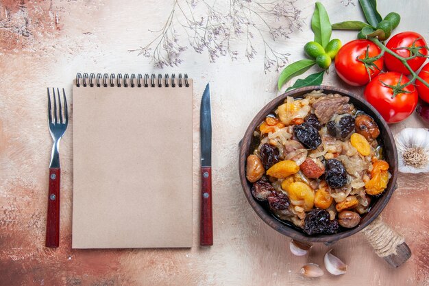 Free photo top close-up view pilaf tomatoes garlic bowl of pilaf on the board fork knife cream notebook