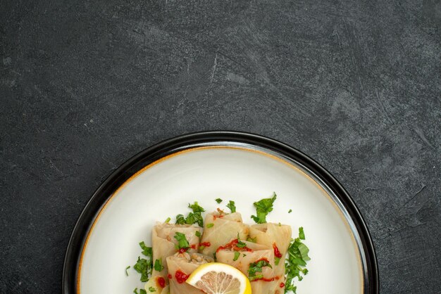 Free photo top close-up view plate of appetizing dish stuffed cabbage with herbs lemon and sauce on a white plate on black surface