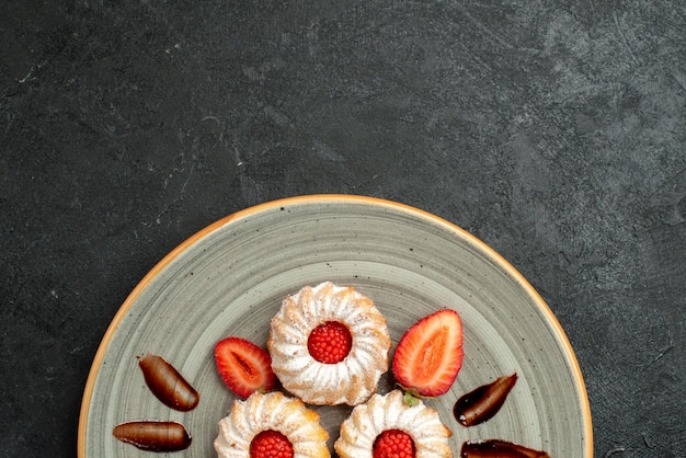 Free photo top close-up view plate of cookies plate of appetizing cookies with chocolate and strawberry on dark table table