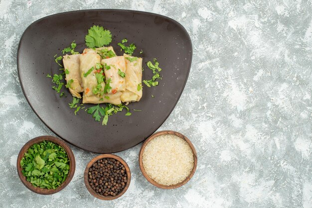 Top close-up view plate of food plate of stuffed cabbage and plates of black papper rice and herbs on the left side of the table