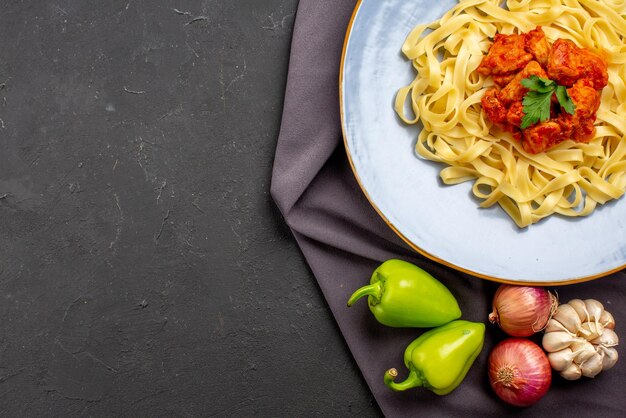 Top close-up view plate of pasta appetizing pasta with meat and herbs next to the onion green ball pepper on the purple tablecloth