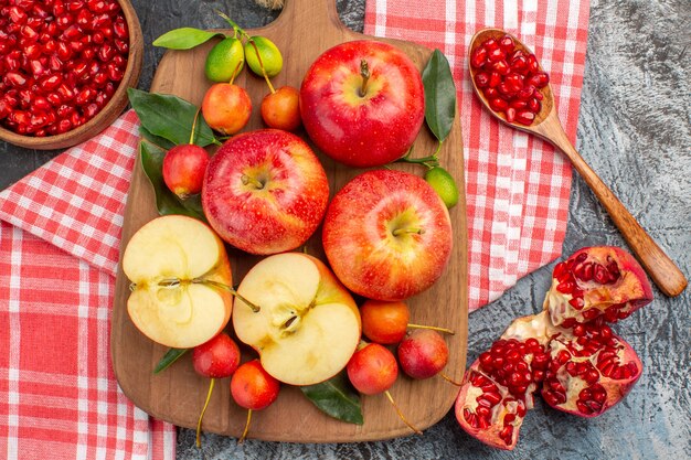 Top close-up view pomegranate apples cherries on the board on the tablecloth bowl of pomegranate