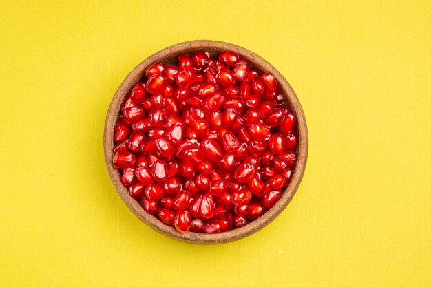 Top close-up view pomegranate bowl of seeds of the appetizing pomegranate on the yellow table