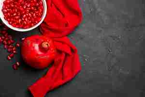 Free photo top close-up view pomegranate pomegranate next to the pomegranate seeds in the bowl red tablecloth