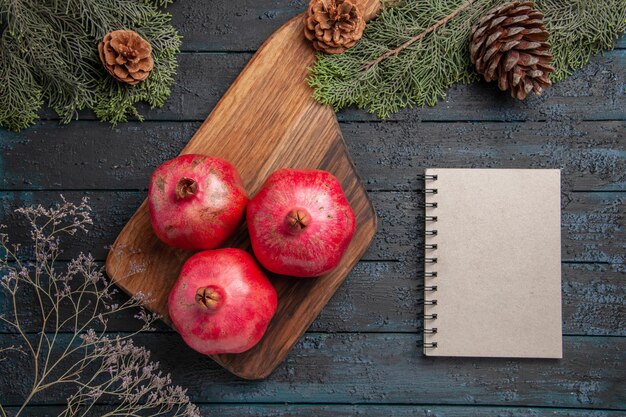 Top close-up view pomegranates and notebook red pomegranates on kitchen board next to white notebook and spuce branches with cones