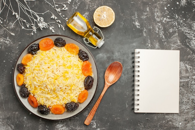 Top close-up view rice plate of rice with dried fruits lemon spoon oil notebook