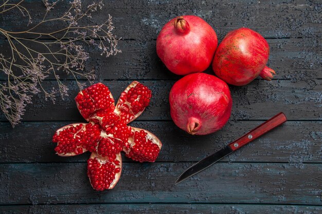 Top close-up view ripe pomegranates ripe pilled pomegranate between three pomegranates tree branches and knife on dark background