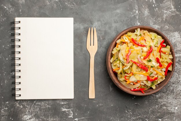 Top close-up view salad an appetizing vegetable salad in the bowl wooden fork notebook