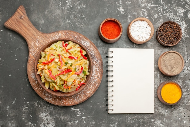 Top close-up view salad white notebook vegetable salad on the board bowls of colorful spices