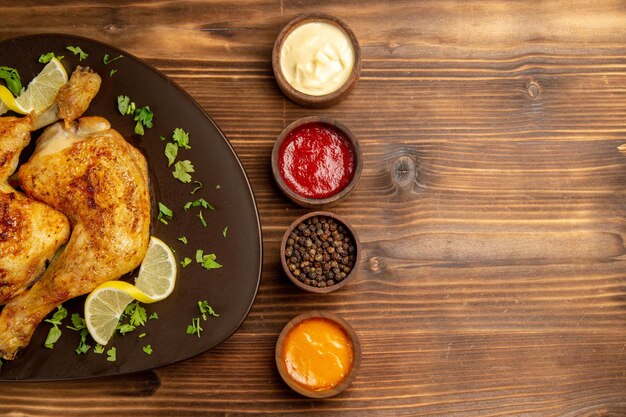 Top close-up view sauces and chicken bowls of colorful sauces black pepper and french fries and the plate of chicken legs with herbs and lemon on the table