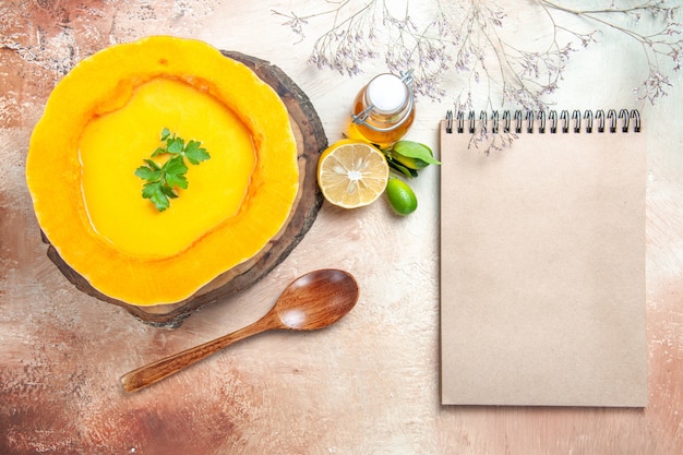 Top close-up view a soup pumpkin soup with herbs on the board spoon oil lemon cream notebook