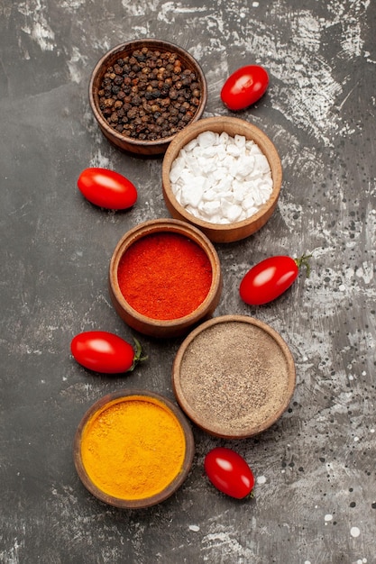 Free photo top close-up view spices five bowls of colorful spices and tomatoes on the dark table