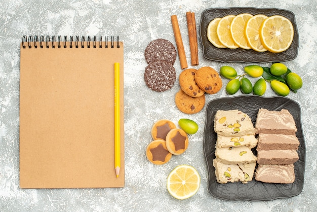 Top close-up view sweets cookies sunflower seed halva citrus fruits cinnamon pencil notebook