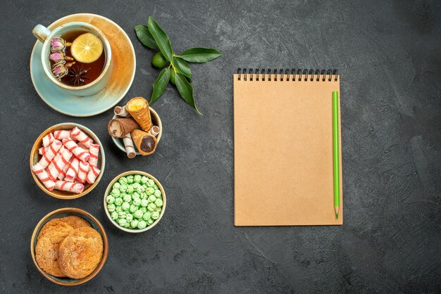 Top close-up view sweets a cup of tea citrus fruits cookies waffles candies cream notebook pencil