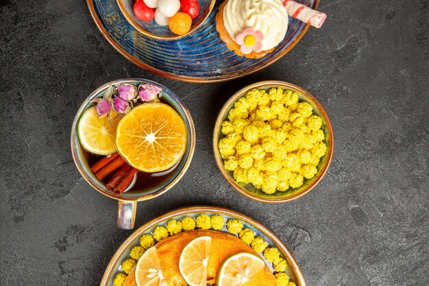 흰색 크림이 든 컵케이크 옆에 오렌지 조각이 있는 식욕을 돋우는 케이크와 시나몬 스틱이 든 차 한 잔 테이블에 노란색 과자 그릇