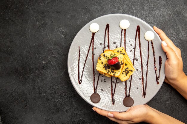 손에 초콜릿 소스와 초콜릿 덮인 딸기가 있는 케이크의 클로즈업 보기 과자 접시