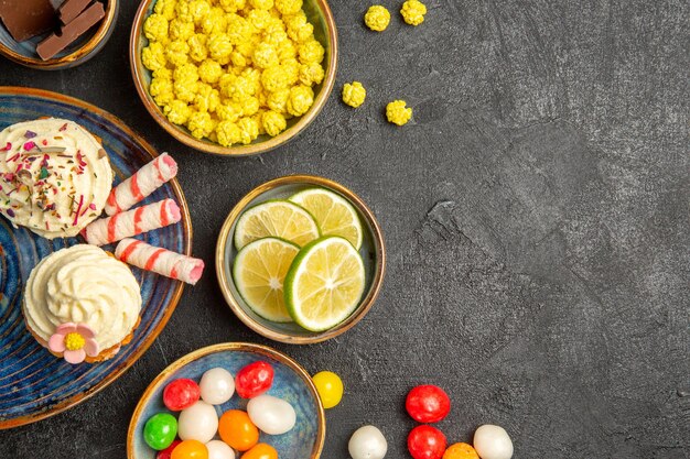 Top close-up view sweets on the table blue saucer of cupcakes and bowls of chocolate limes colorful sweets on the left side of the table