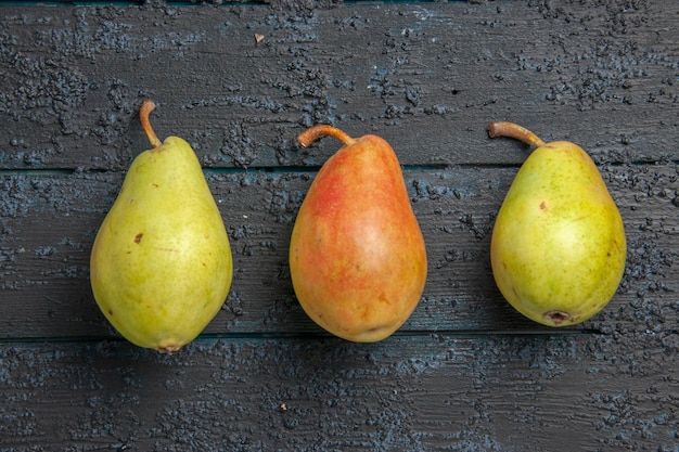 Top close-up view three pears on table two green pears and one red-yellow pear in the center of grey table