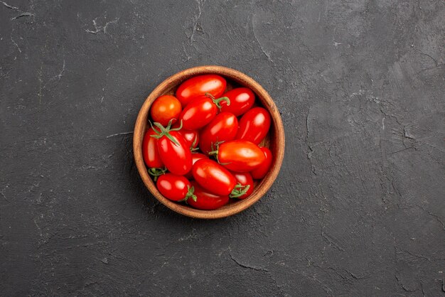 Top close-up view tomatoes in bowl ripe red tomatoes in bowl in the center of the dark table