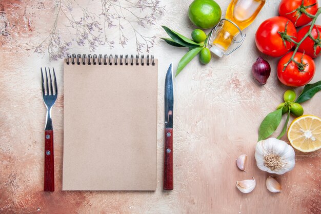 Top close-up view tomatoes tomatoes garlic bottle of oil lemon leaves cream notebook knife fork