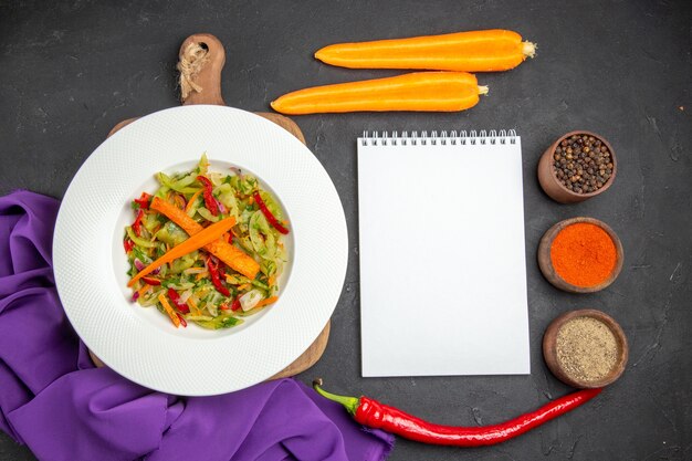 Top close-up view vegetables salad on the cutting board notebook spices carrots