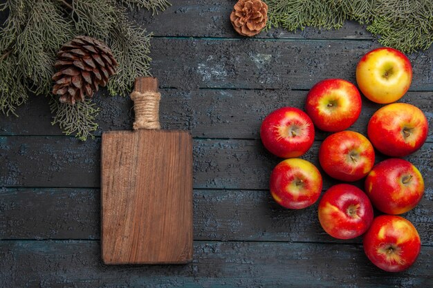 Top close view apples and board nine apples and cutting board under the tree branches with cones