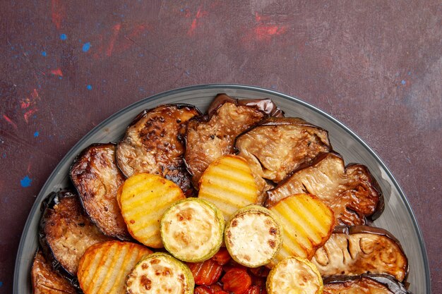 Top close view baked vegetables potatoes and eggplants fresh off the oven on dark space