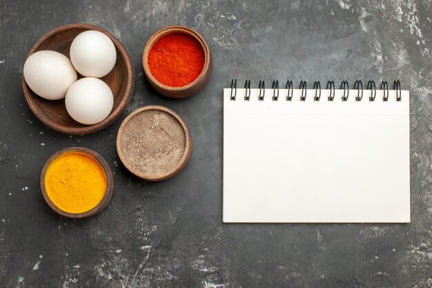 Top close view of bowl of eggs notepad and herbs on dark grey table