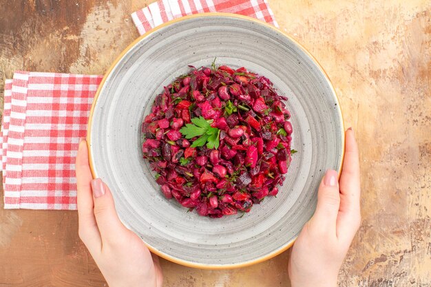 Top close view of bowl of a red salad with greens on it on a checked napkin on a wooden backgorund