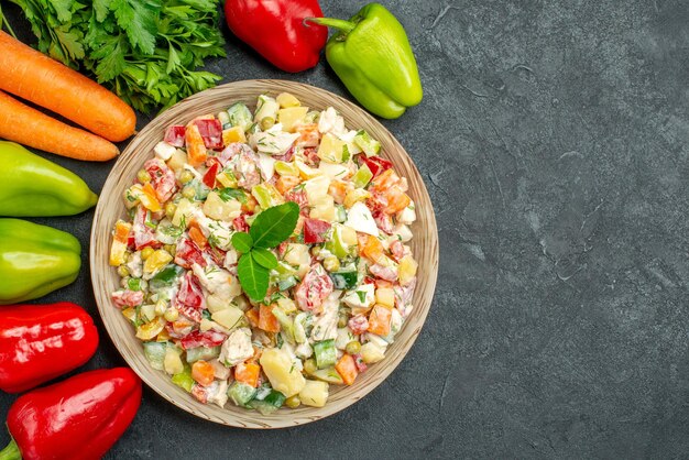 Top close view of bowl of vegetable salad with carrots greens and bell peppers on side on dark grey table