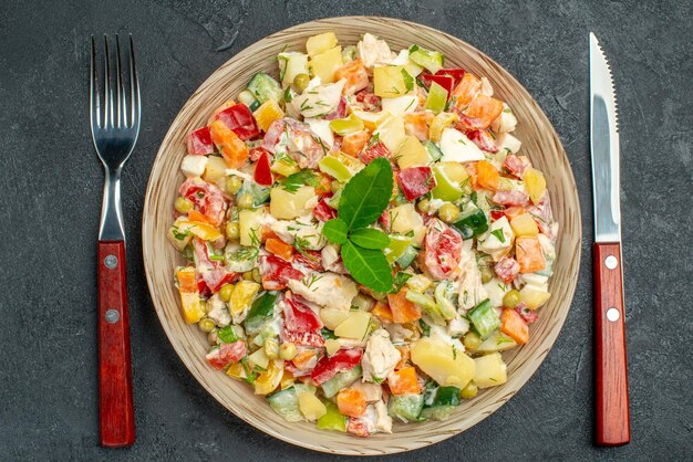 濃い灰色の背景にフォークとナイフが付いている野菜サラダのボウルの上面拡大図
