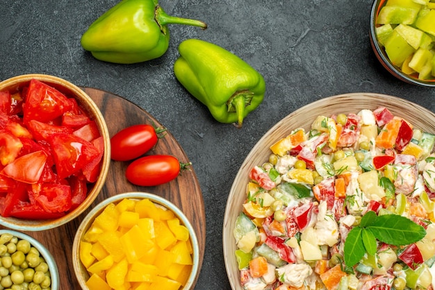 Top close view of bowl of vegetable salad with plate stand of vegetables on side on dark grey background