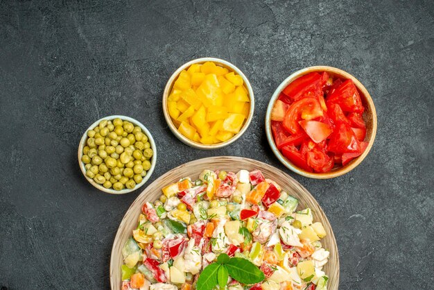 Top close view of bowl of vegetable salad with vegs on side on dark grey background