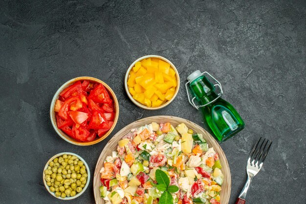 Top close view of bowl of veggie salad with vegetables oil bottle and fork on dark background