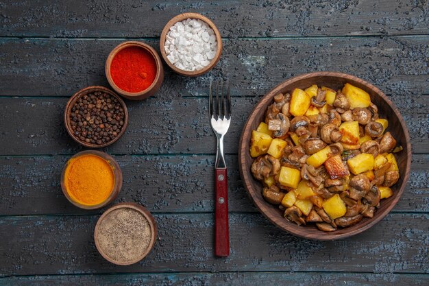 Top close view brown bowl of food a bowl of potatoes and mushrooms next to the fork and different colorful spices