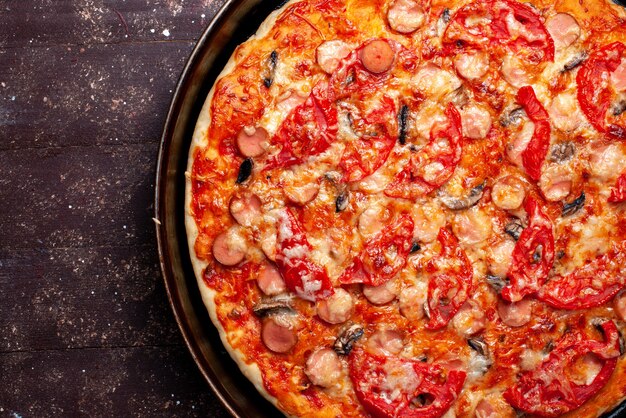 Вид сверху сырной томатной пиццы с оливками и сосисками внутри сковороды на коричневом столе, пицца, еда, фаст-фуд, сырная колбаса