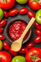 Free photo top close view cherry red and green tomatoes around a bowl with ketchup and a wooden spoon on dark ground