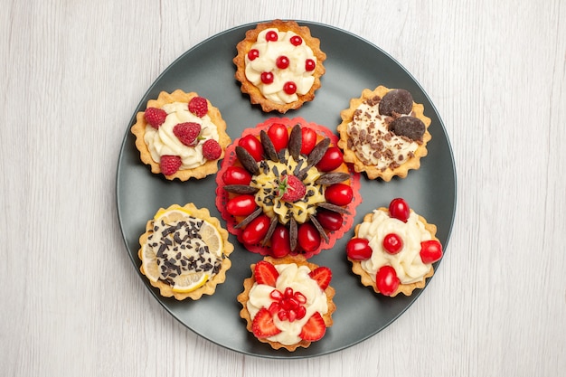 Top close view chocolate cake rounded with berry tarts in the grey plate at the center of the white wooden table