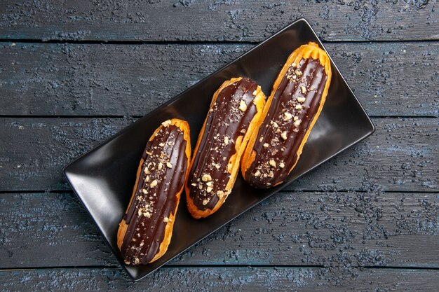 Top close view chocolate eclairs on rectangle plate on dark wooden table with free space