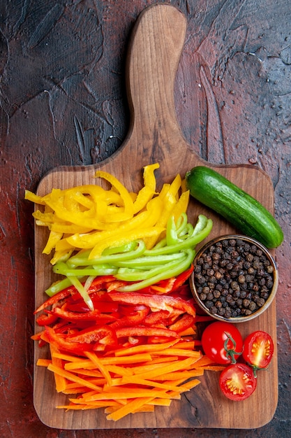 Top close view colorful cut peppers black pepper tomatoes cucumber on cutting board on dark red table