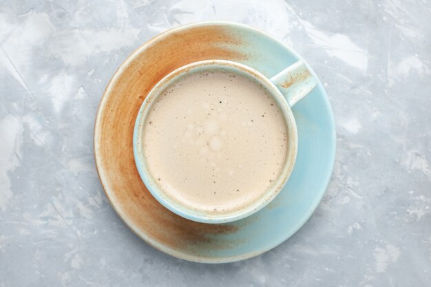 白い机の上のカップの中に牛乳が入ったコーヒーのトップクローズビューカップはコーヒーミルクデスクの色を飲みます