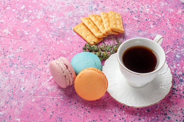 Top close view of cup of tea with yummy french macarons on the pink wall