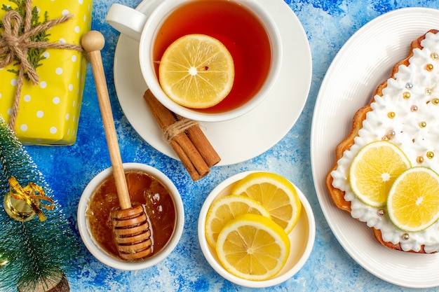 Top close view cup of tea xmas gift honey in bowl lemon slices cake on plate on blue table