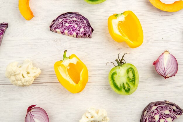 Top close view cut vegetables red cabbage green tomato pumpkin red onion yellow bell pepper caulifower on white surface